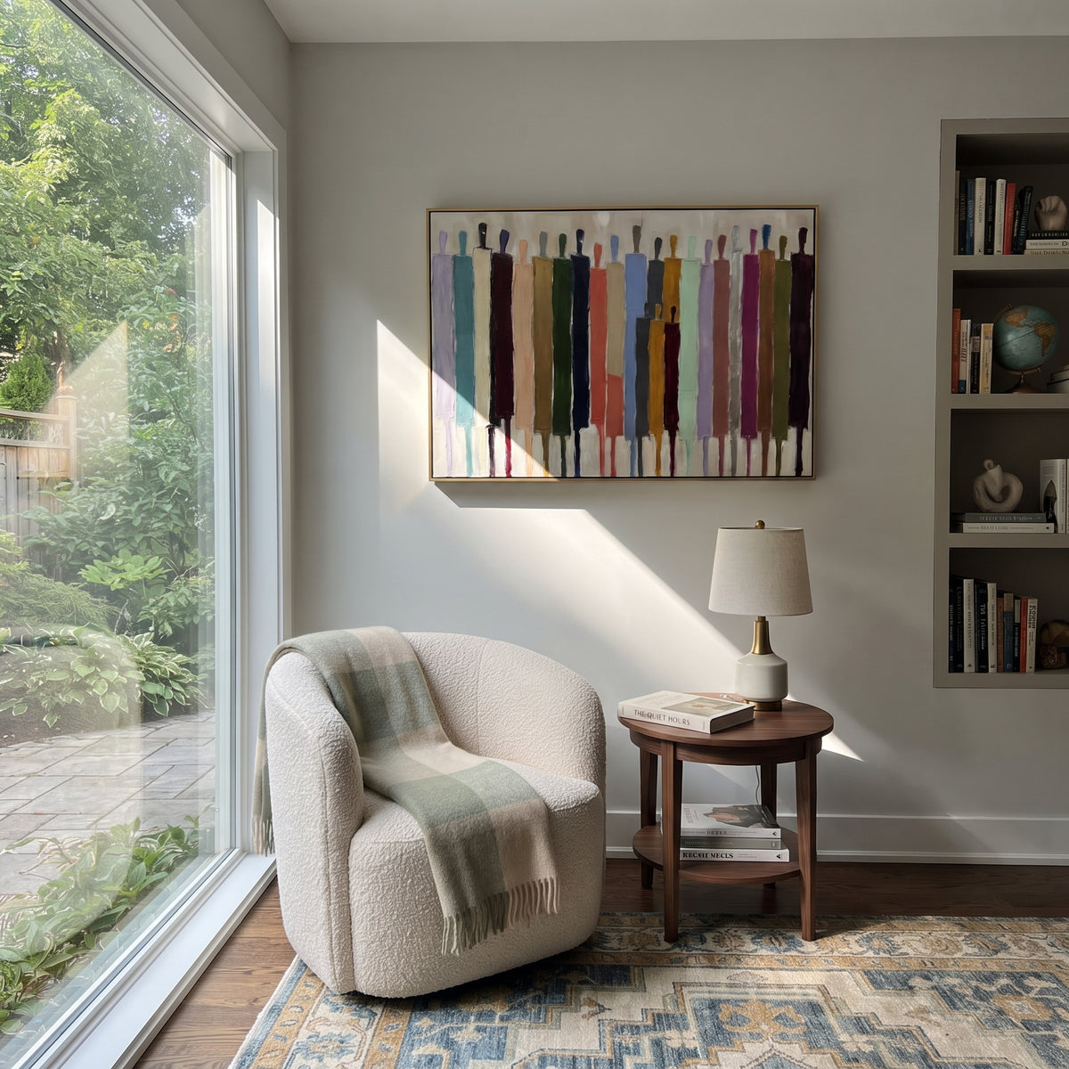 Bright Procession Across White – colorful elongated figures painting, displayed beside a quiet reading nook