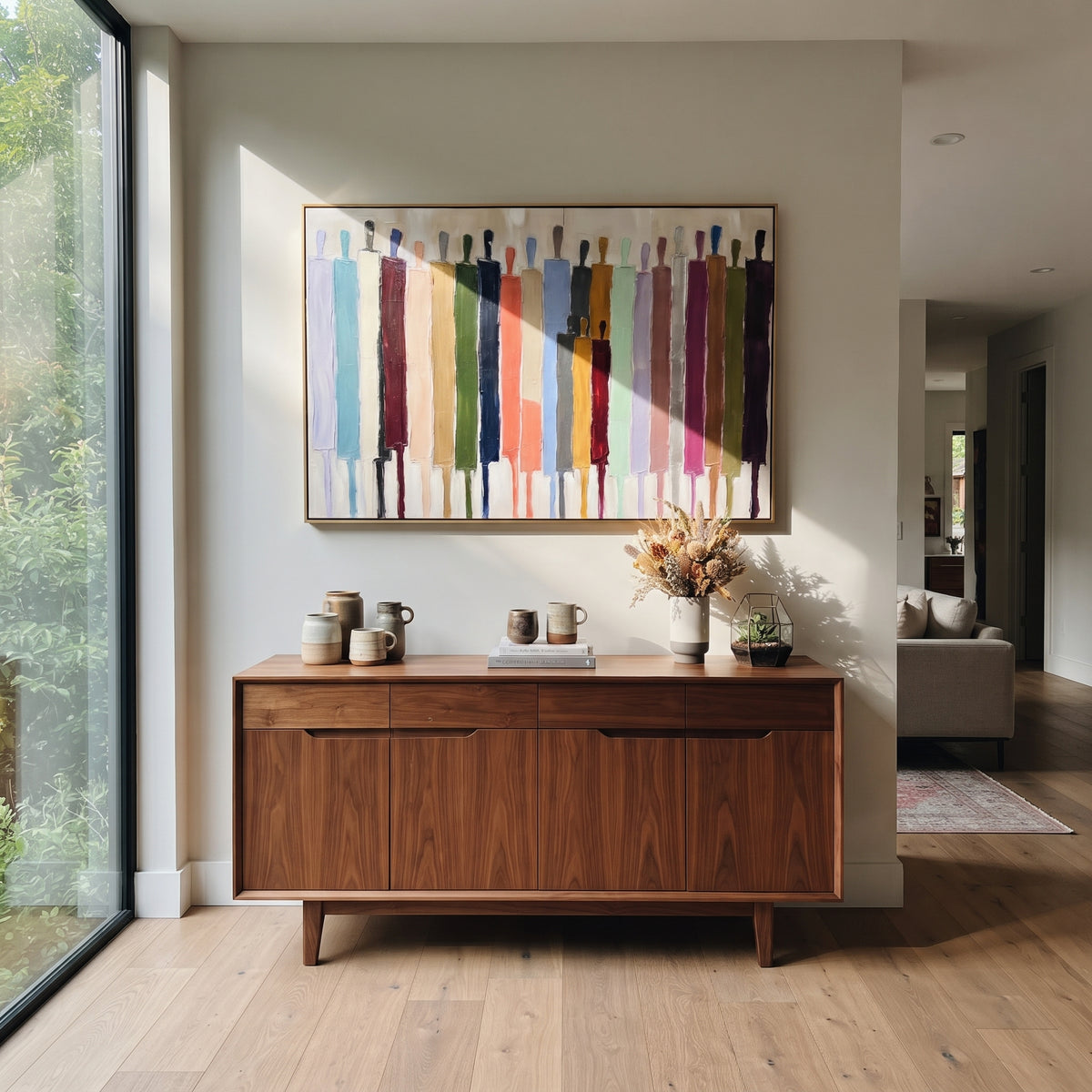 Bright Procession Across White – colorful elongated figures painting, displayed above a walnut sideboard