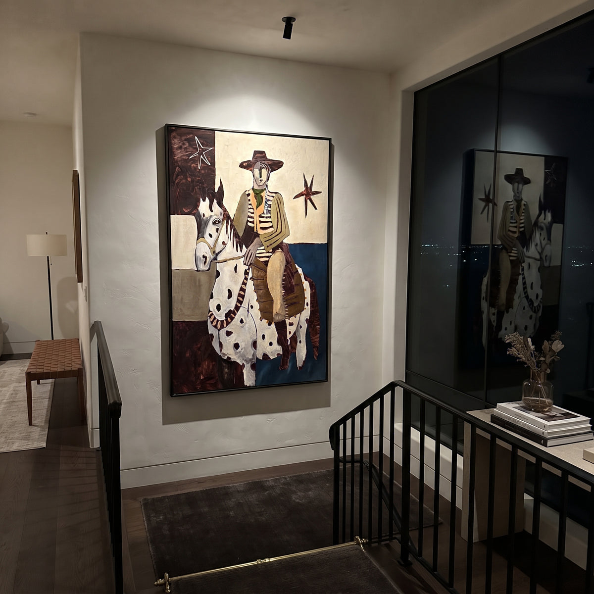 The Spotted Mare Holds Dawn - cowboy on white pinto horse painting, modern figurative vertical textured wall art - displayed beside a leather chair